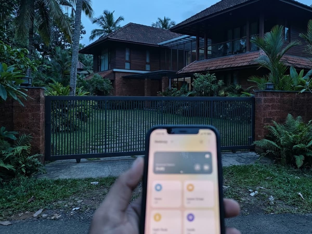 Hand using a phone app to open the sliding gate at a Kerala house at dusk
