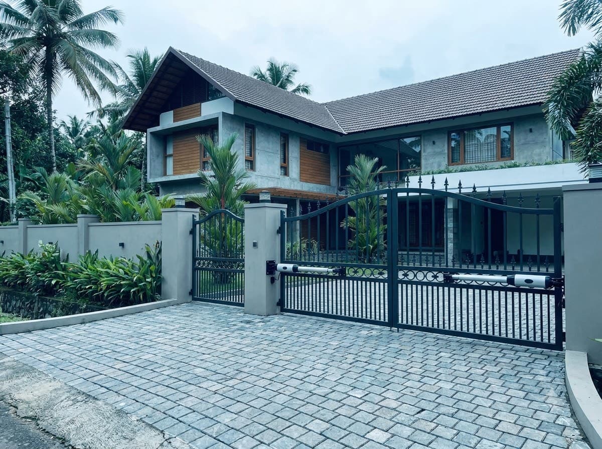 Two-leaf swing gate fitted with arm motors at a Kerala house with a paved driveway